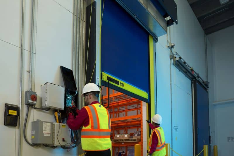 Two workers performing maintenance on a coiling door