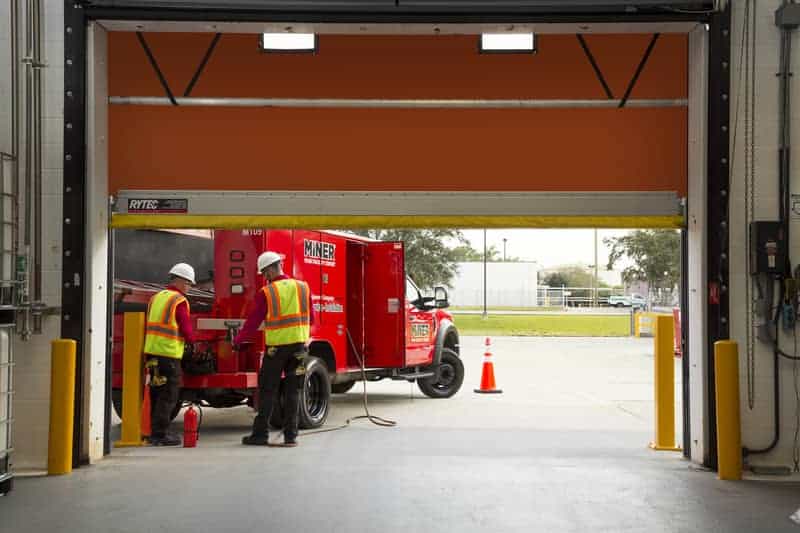 Two workers in front of a coiling door, performing work at their truck